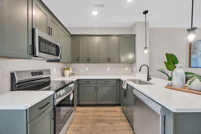 kitchen featuring light hardwood / wood-style floors, kitchen peninsula, stainless steel appliances, pendant lighting, and sink