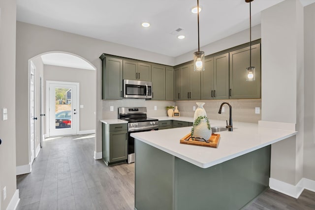 kitchen featuring stainless steel appliances, sink, hanging light fixtures, kitchen peninsula, and light hardwood / wood-style flooring