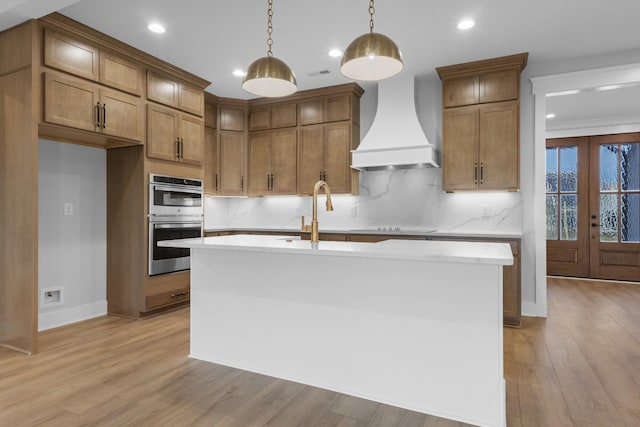 kitchen with pendant lighting, french doors, a kitchen island with sink, and custom range hood