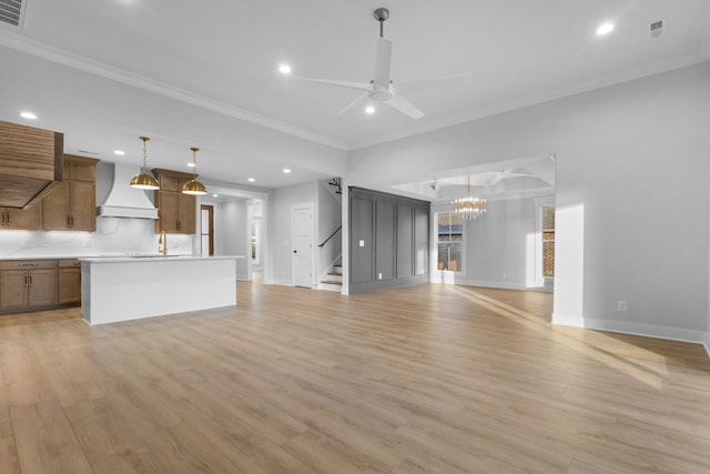 unfurnished living room with ceiling fan with notable chandelier, light wood-type flooring, crown molding, and sink