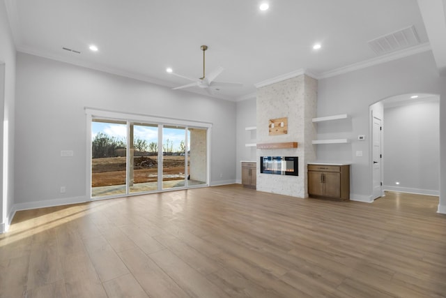 unfurnished living room featuring built in shelves, ceiling fan, crown molding, and a stone fireplace