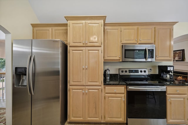 kitchen with appliances with stainless steel finishes, dark stone counters, light brown cabinetry, and lofted ceiling