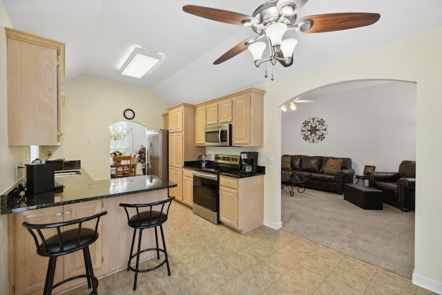 kitchen with light carpet, stainless steel appliances, kitchen peninsula, light brown cabinetry, and lofted ceiling