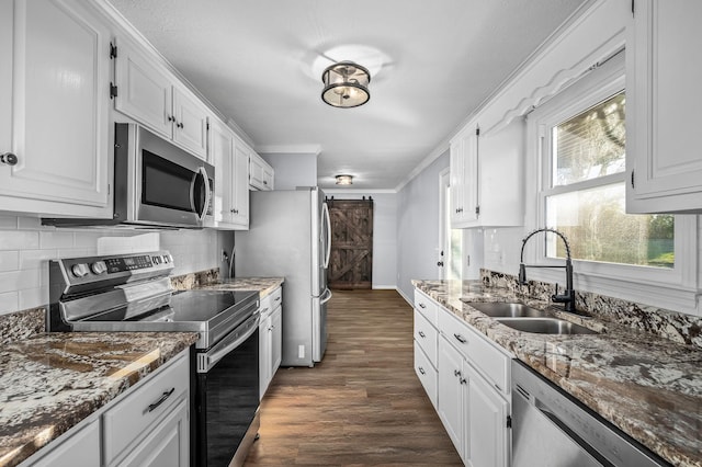 kitchen featuring sink, white cabinets, dark stone counters, a barn door, and appliances with stainless steel finishes