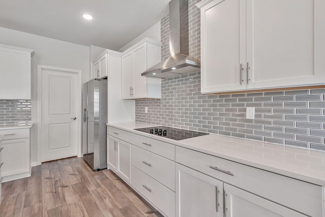 kitchen featuring stainless steel fridge with ice dispenser, wall chimney range hood, tasteful backsplash, black electric cooktop, and white cabinets