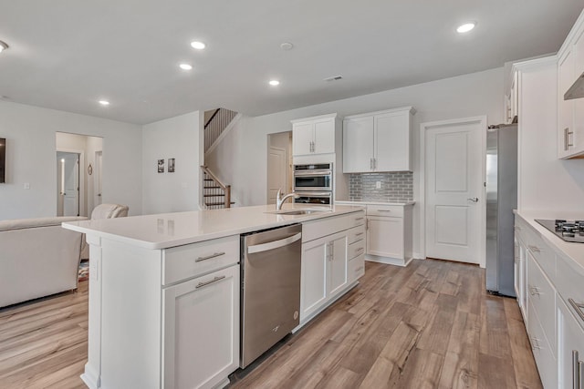 kitchen featuring stainless steel appliances, a center island with sink, white cabinets, and tasteful backsplash