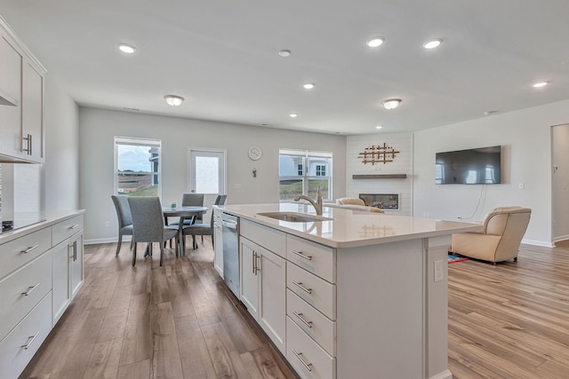 kitchen featuring sink, white cabinetry, dishwasher, a large fireplace, and a kitchen island with sink