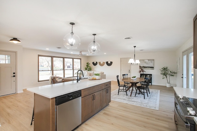 kitchen featuring a kitchen island with sink, appliances with stainless steel finishes, hanging light fixtures, light hardwood / wood-style floors, and sink