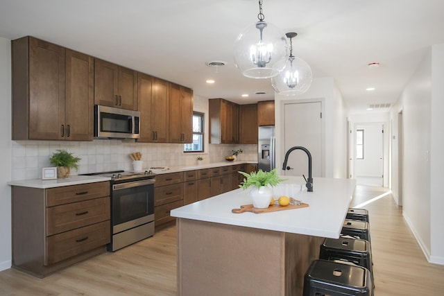 kitchen with a kitchen breakfast bar, appliances with stainless steel finishes, an island with sink, pendant lighting, and decorative backsplash