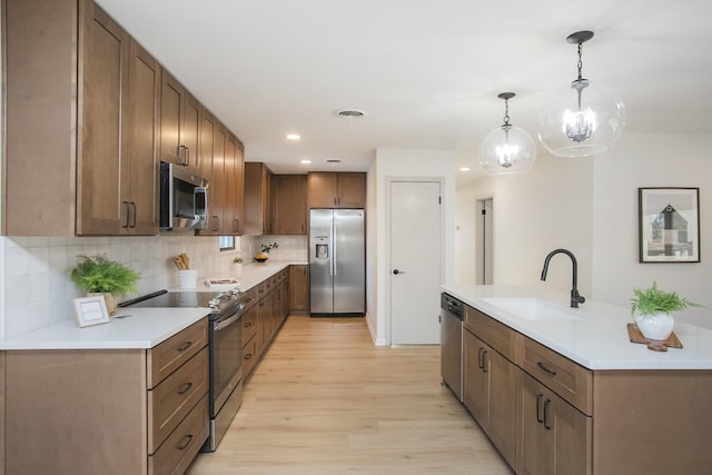 kitchen featuring light hardwood / wood-style floors, stainless steel appliances, sink, decorative light fixtures, and backsplash