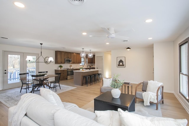 living room featuring sink, light wood-type flooring, and ceiling fan with notable chandelier