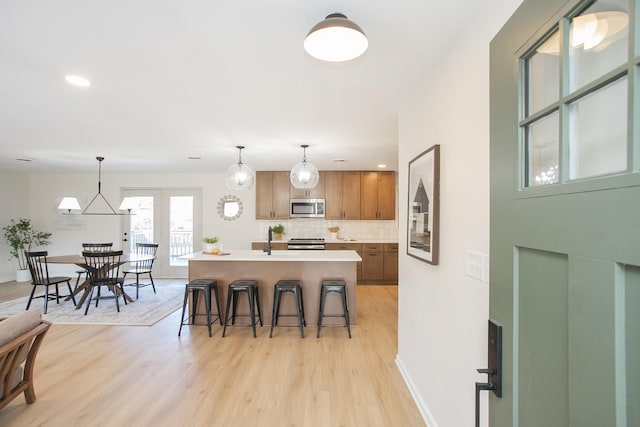 kitchen featuring hanging light fixtures, tasteful backsplash, a kitchen island with sink, a breakfast bar area, and appliances with stainless steel finishes