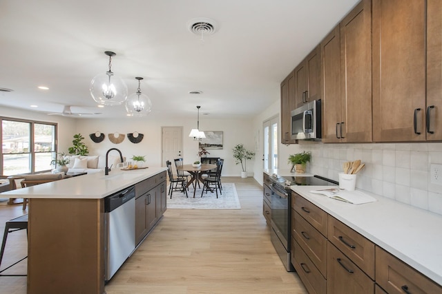 kitchen with a kitchen island with sink, a breakfast bar area, light hardwood / wood-style floors, stainless steel appliances, and hanging light fixtures