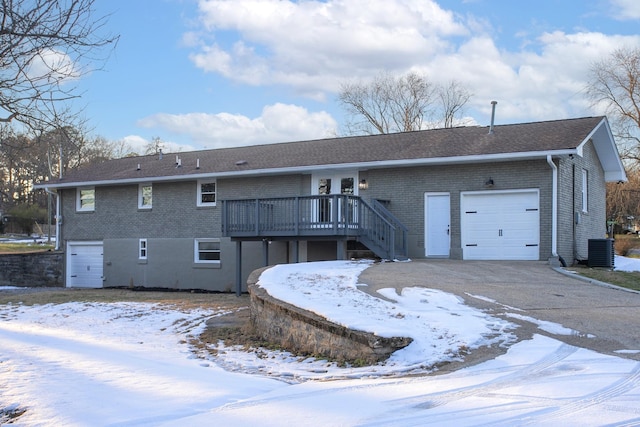 snow covered house featuring cooling unit, a garage, and a wooden deck