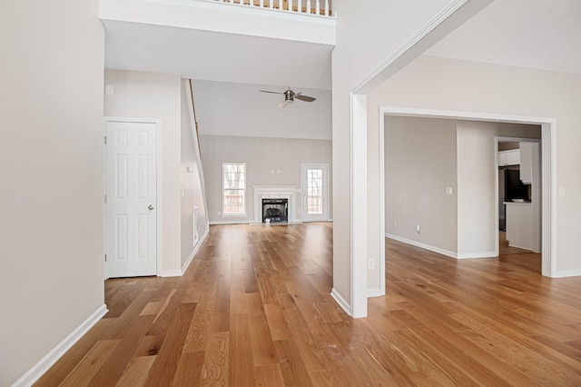 unfurnished living room featuring a high ceiling, light wood-type flooring, and ceiling fan