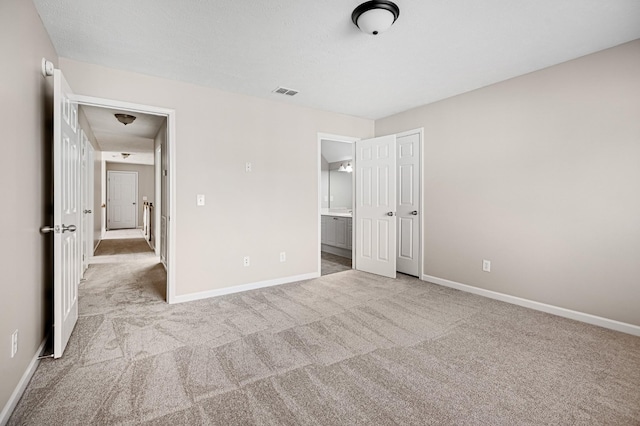 unfurnished bedroom featuring ensuite bath, a closet, and light carpet