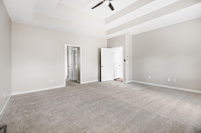 carpeted spare room with a raised ceiling and ceiling fan