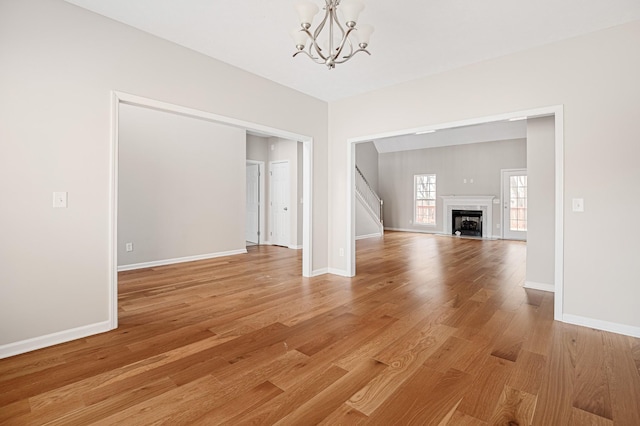 unfurnished living room with a high end fireplace, light wood-type flooring, and a notable chandelier