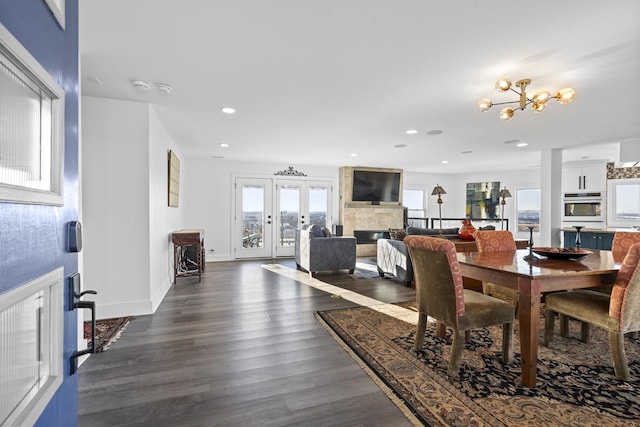 dining space featuring a large fireplace, an inviting chandelier, french doors, and dark hardwood / wood-style flooring