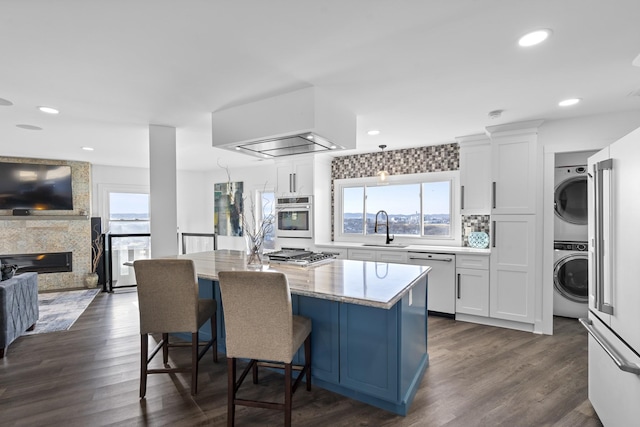 kitchen featuring sink, white cabinetry, light stone counters, stacked washer / drying machine, and appliances with stainless steel finishes