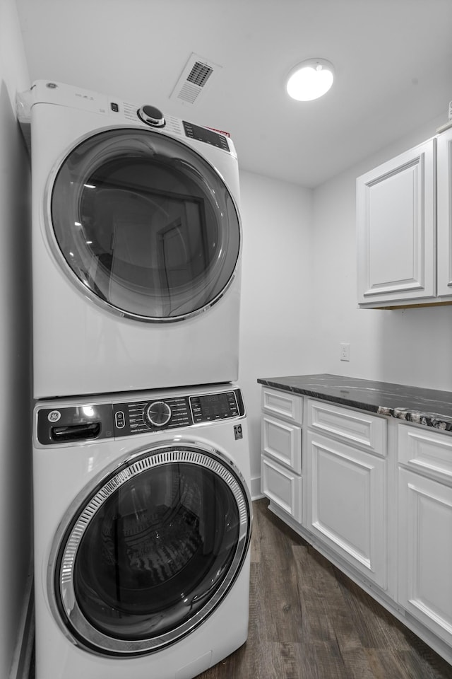 clothes washing area featuring cabinets, stacked washer / dryer, and dark hardwood / wood-style floors