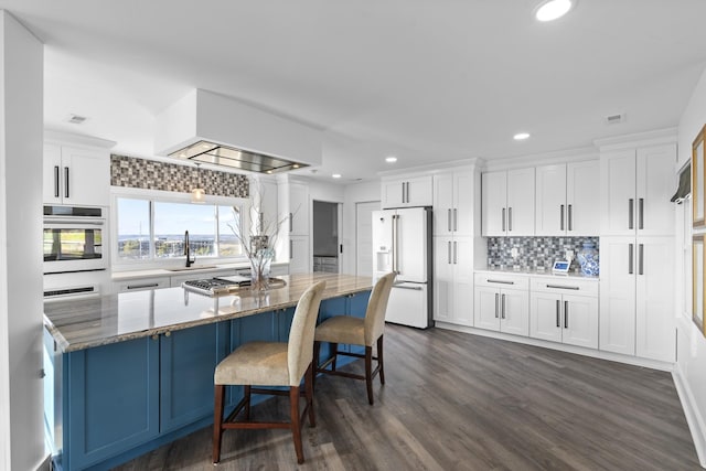 kitchen with white appliances, decorative backsplash, a kitchen island, white cabinetry, and dark stone counters