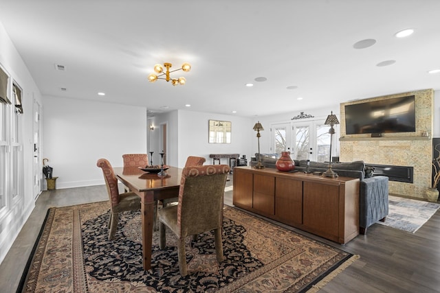 dining room featuring dark wood-type flooring, french doors, a tile fireplace, and a chandelier