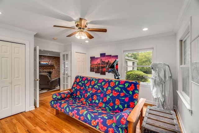 living room with a brick fireplace, ceiling fan, crown molding, and wood-type flooring