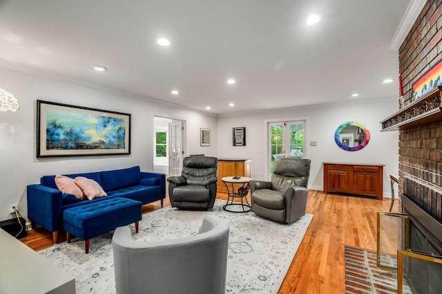 living room with a brick fireplace, french doors, ornamental molding, and light hardwood / wood-style flooring