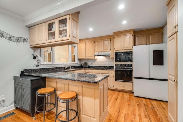 kitchen featuring light wood-type flooring, kitchen peninsula, black appliances, a breakfast bar, and crown molding