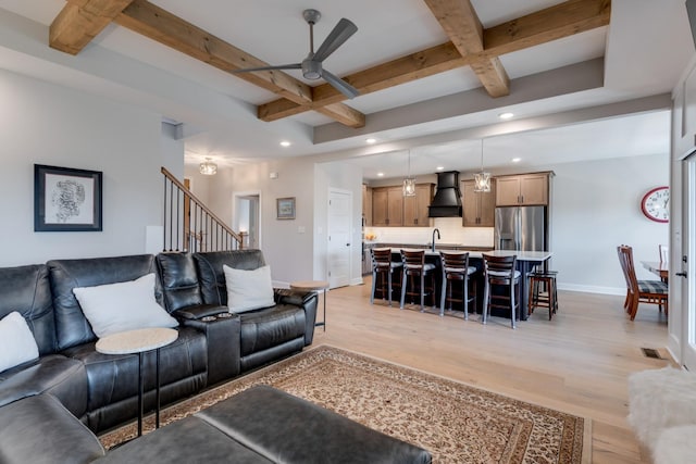 living room with sink, light wood-type flooring, ceiling fan, beam ceiling, and coffered ceiling