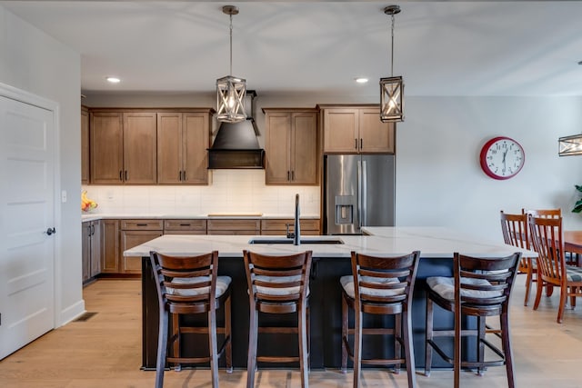 kitchen featuring stainless steel fridge with ice dispenser, sink, a center island with sink, and custom range hood