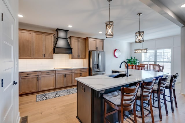 kitchen with custom exhaust hood, sink, a kitchen breakfast bar, stainless steel fridge, and a kitchen island with sink