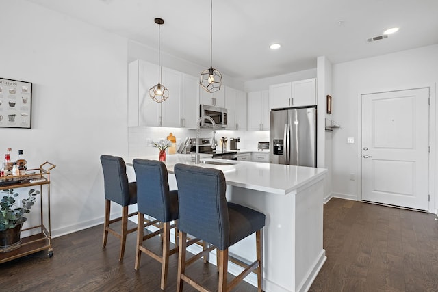 kitchen with appliances with stainless steel finishes, kitchen peninsula, a kitchen bar, white cabinets, and decorative light fixtures