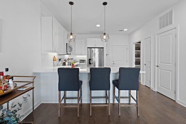 kitchen with kitchen peninsula, hanging light fixtures, stainless steel appliances, a breakfast bar, and white cabinets