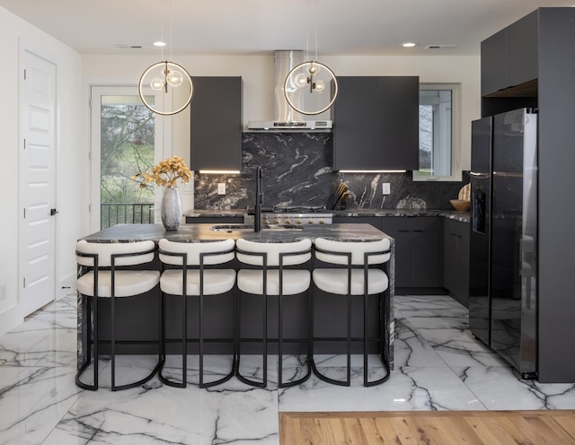 kitchen with sink, wall chimney exhaust hood, a kitchen bar, backsplash, and stainless steel fridge