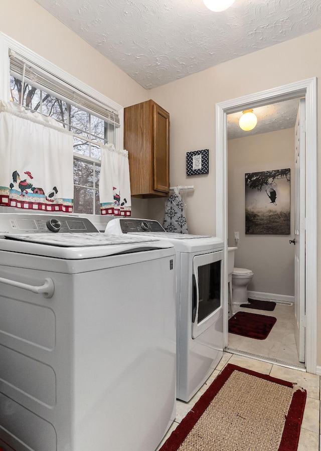 clothes washing area with separate washer and dryer, cabinets, a textured ceiling, and light tile patterned floors