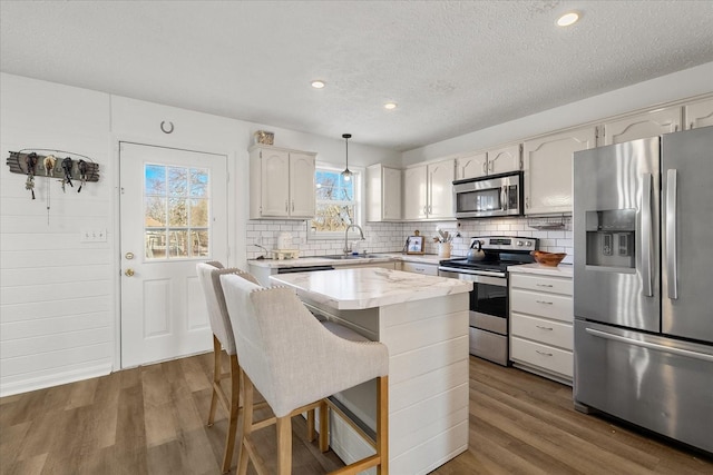 kitchen featuring appliances with stainless steel finishes, a kitchen island, white cabinetry, sink, and hanging light fixtures