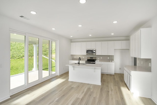 kitchen with sink, white cabinetry, light hardwood / wood-style floors, a center island with sink, and appliances with stainless steel finishes