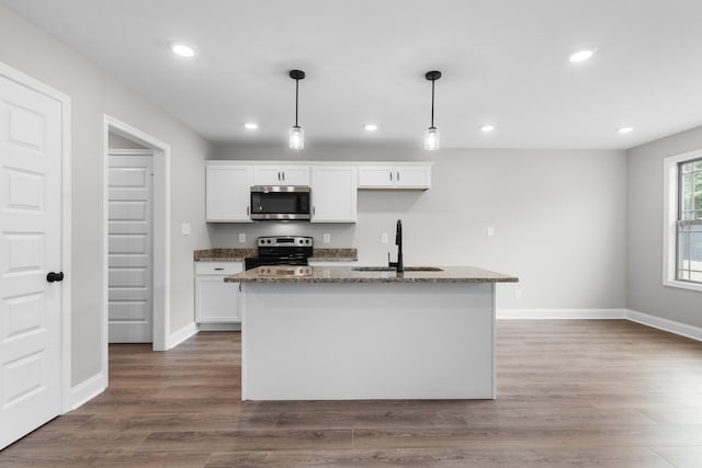 kitchen with a kitchen island with sink, stainless steel appliances, dark stone counters, white cabinetry, and decorative light fixtures