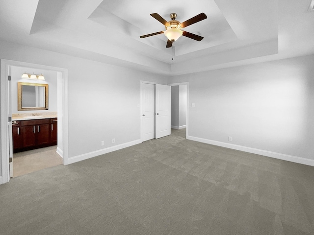 unfurnished bedroom featuring ceiling fan, connected bathroom, a raised ceiling, a closet, and light colored carpet