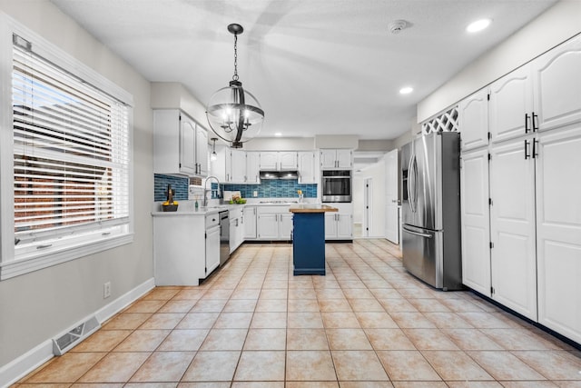 kitchen featuring decorative light fixtures, white cabinets, backsplash, a kitchen island, and appliances with stainless steel finishes