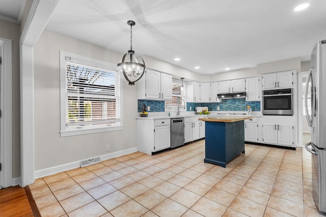 kitchen featuring pendant lighting, a center island, stainless steel appliances, decorative backsplash, and white cabinetry