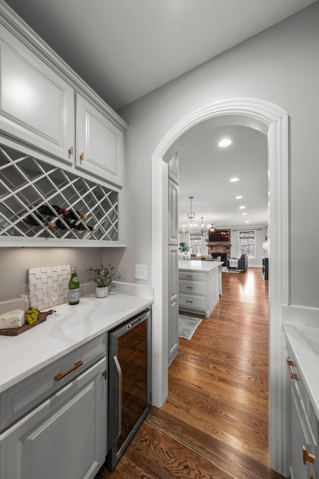 bar featuring decorative backsplash, dark hardwood / wood-style flooring, beverage cooler, and light stone countertops