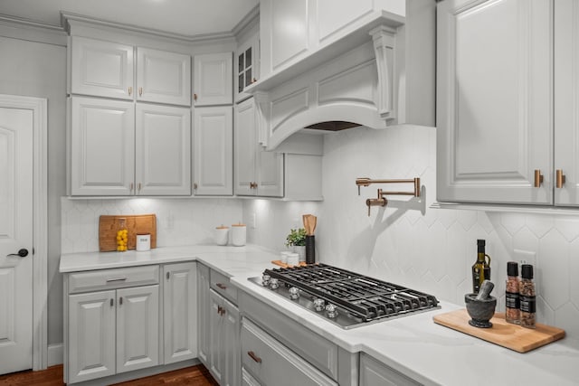 kitchen featuring light stone counters, premium range hood, stainless steel gas cooktop, and backsplash