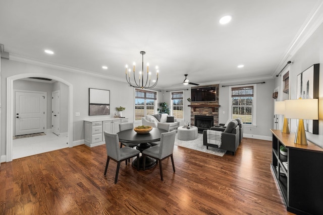 dining room featuring ceiling fan with notable chandelier, hardwood / wood-style flooring, crown molding, and a stone fireplace