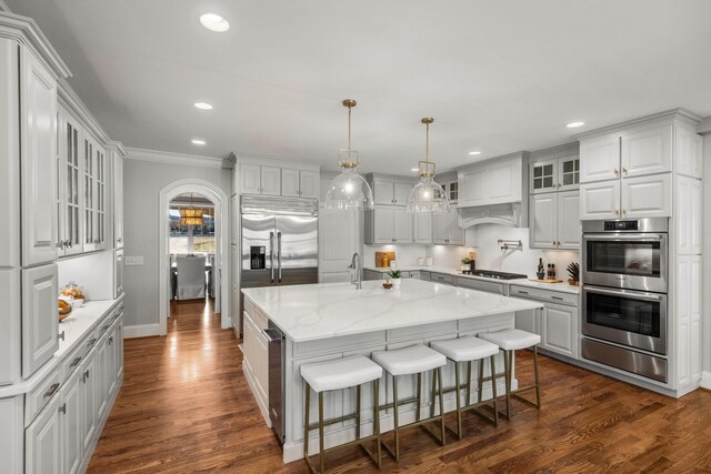 kitchen with a center island with sink, stainless steel appliances, pendant lighting, a kitchen bar, and white cabinets