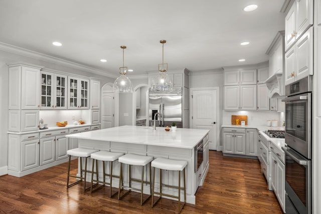 kitchen with built in appliances, white cabinets, and a kitchen island with sink