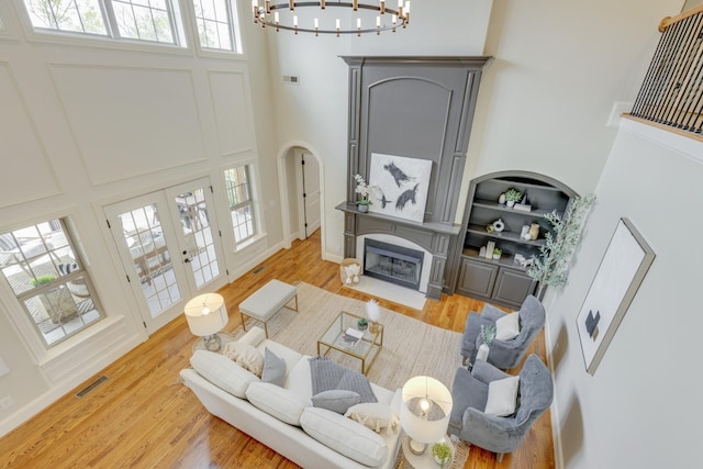 living room with a towering ceiling, light wood-type flooring, french doors, and a chandelier