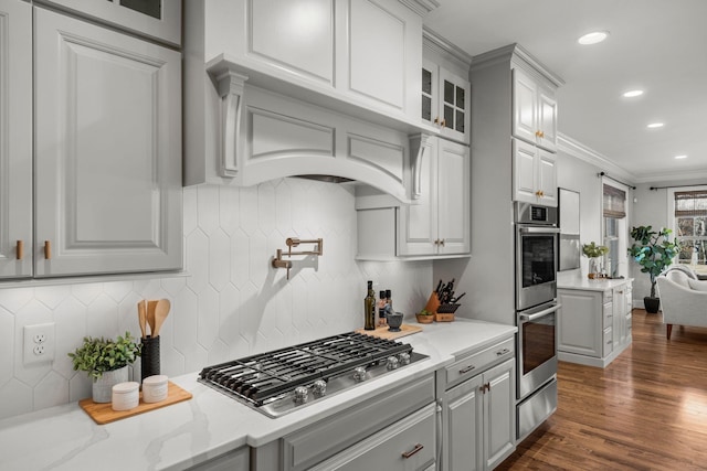 kitchen with stainless steel appliances, ornamental molding, backsplash, and light stone countertops